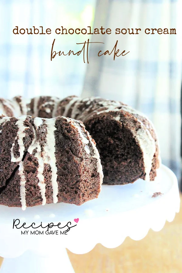 This photo shows Double Chocolate Sour Cream Bundt Cake on a white cake stand with a slice missing, showing the inside of the cake. 