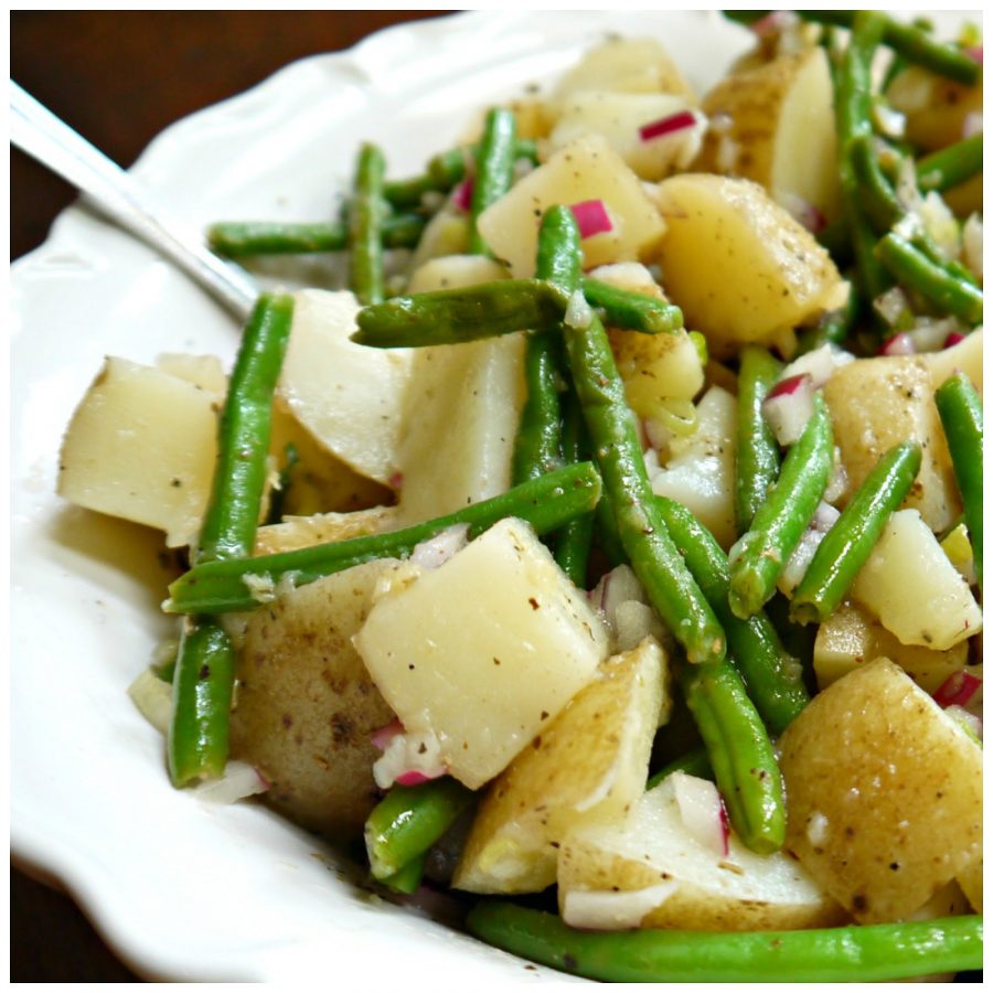 This photo shows potato and green bean salad served in a white bowl with a spoon.