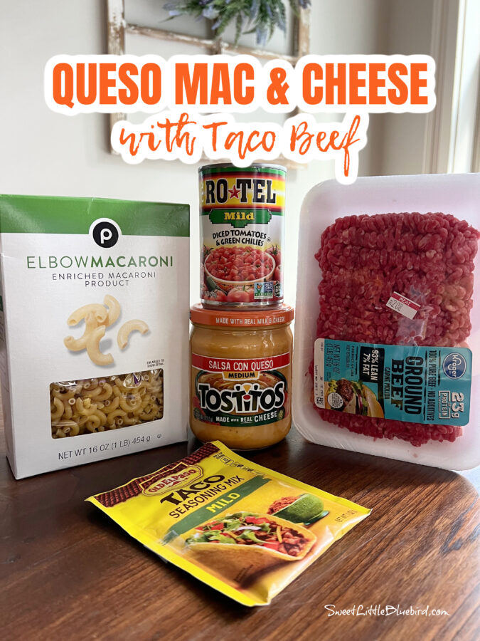 Photo of all the ingredients to make the macaroni and cheese - box of macaroni noodles, can of Rotel, jar of queso, ground beef and a packet of taco seasoning. 