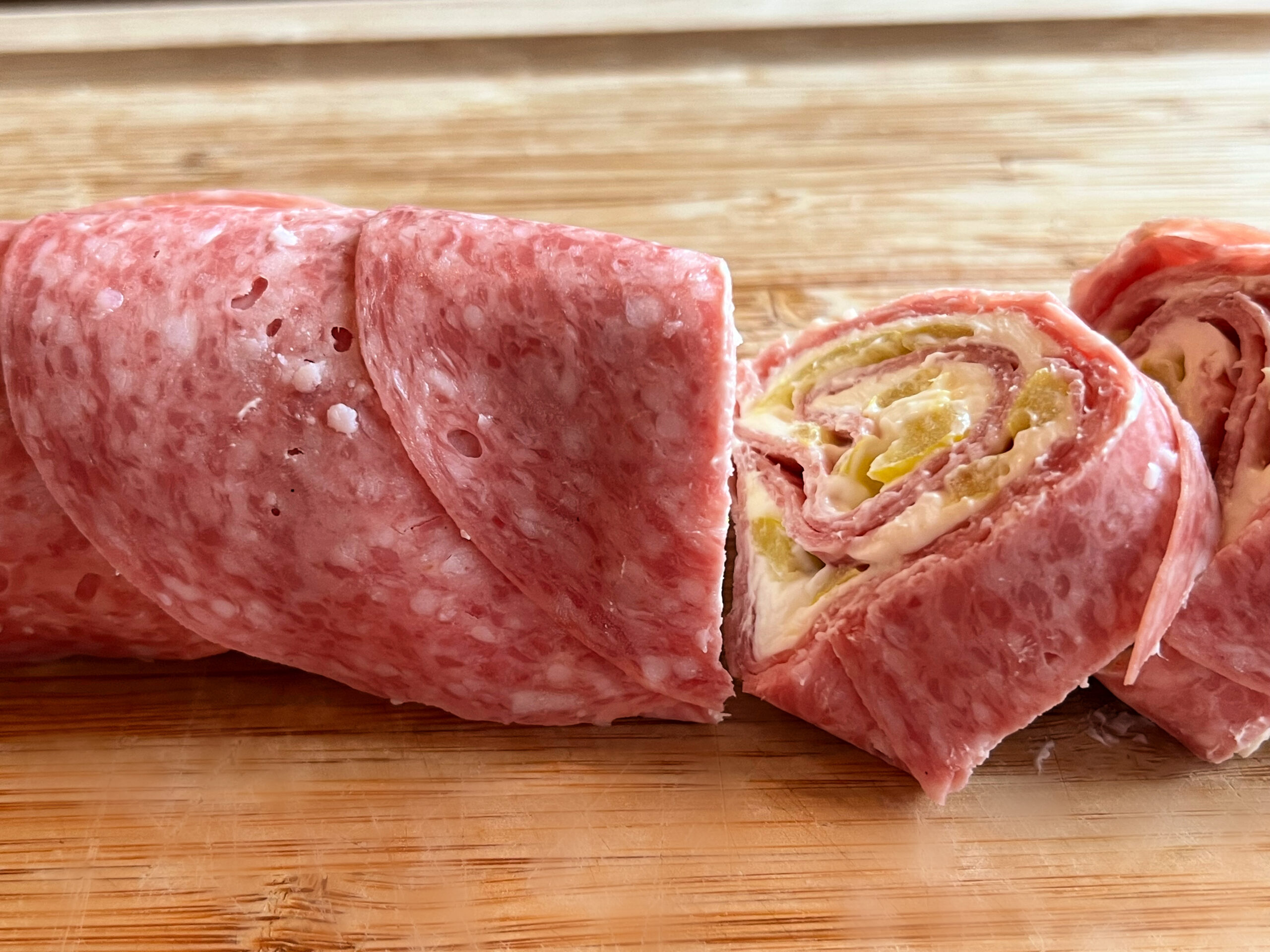 This photo shows the rolled up salami being sliced into round bite size pieces. 