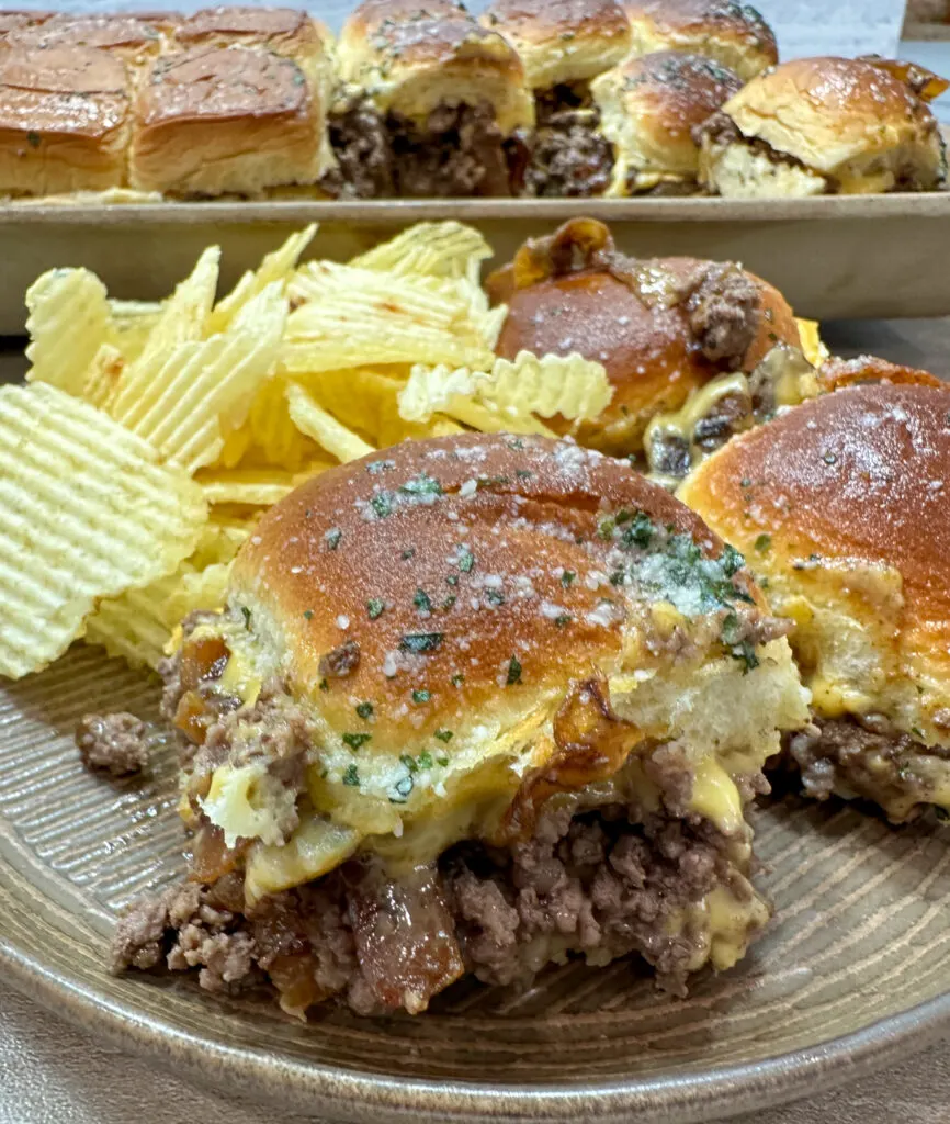 This photo shows two ground beef sliders on a plate served with potato chips. 