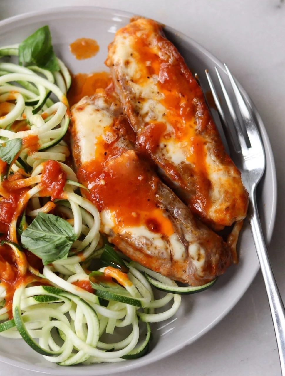 Cheesy Stuffed Sausage Two cheesy stuffed sausages on a white plate with a fork with a side of spiral zucchini.